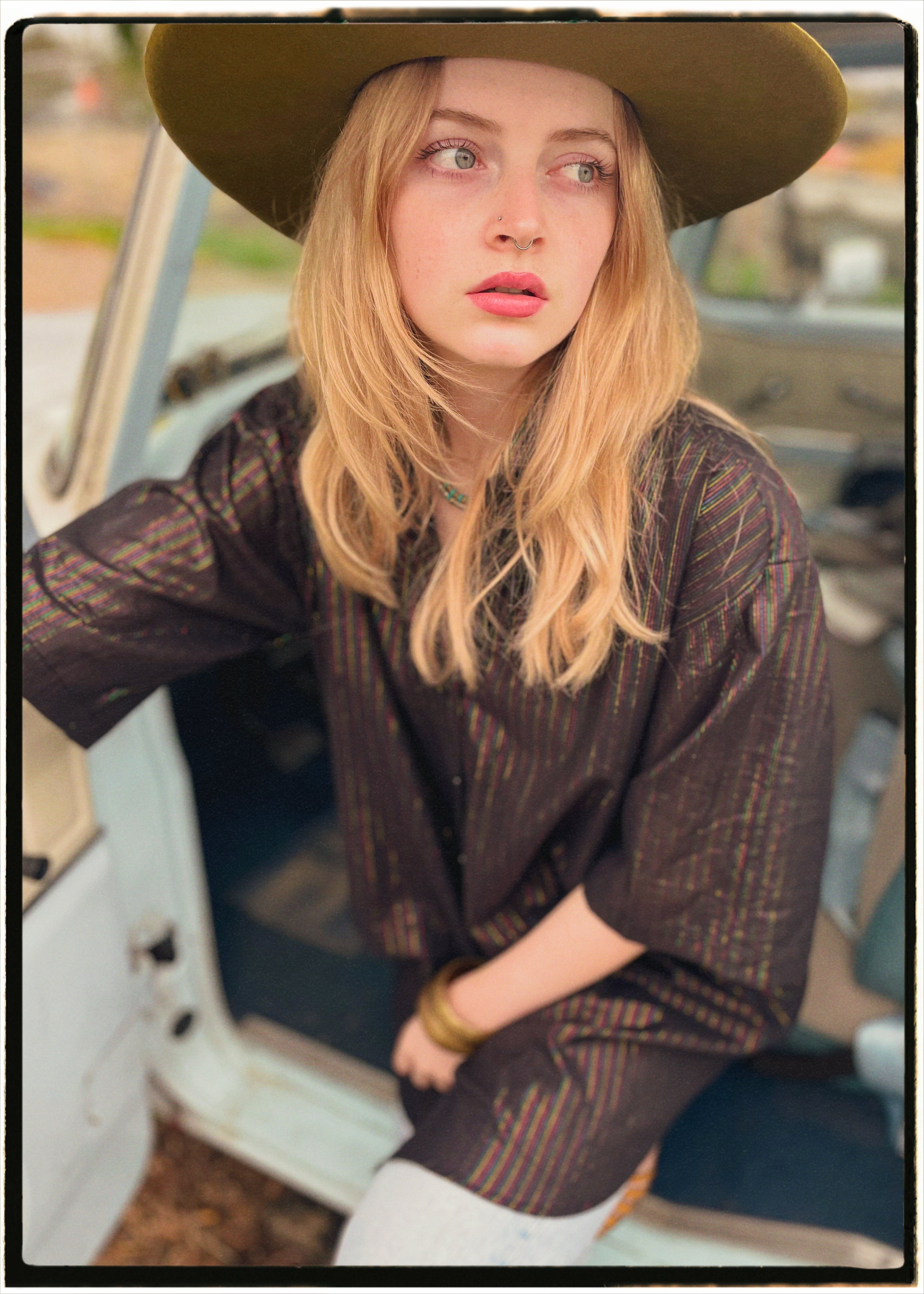 Woman wearing a bohemian style balloon sleeved blouse made from vintage Indian repurposed silk crepe saree sitting in the back of a vintage car with a scenic background