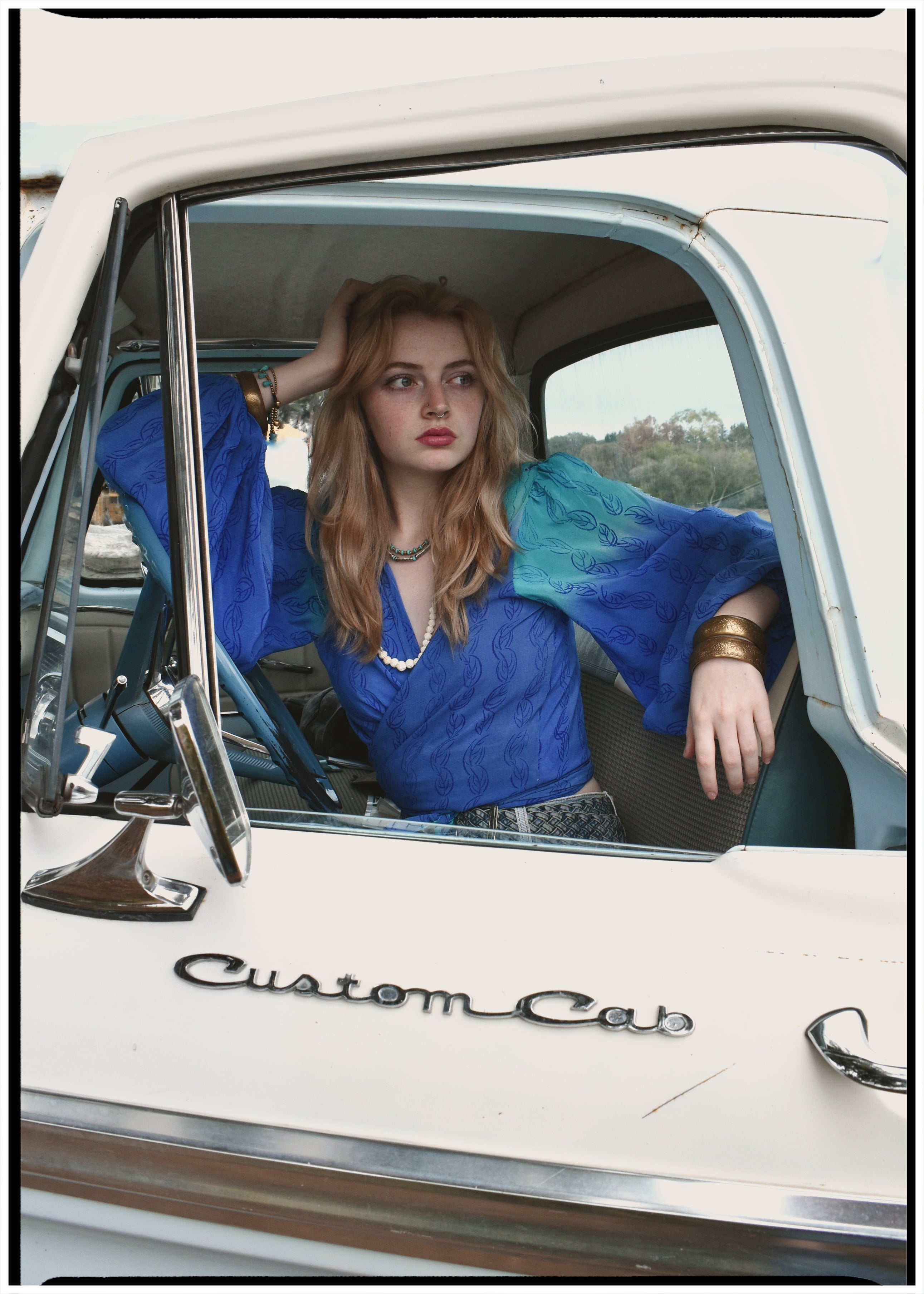 Woman wearing a bohemian style balloon sleeved blouse made from vintage Indian repurposed silk crepe saree sitting in the back of a vintage car with a scenic background