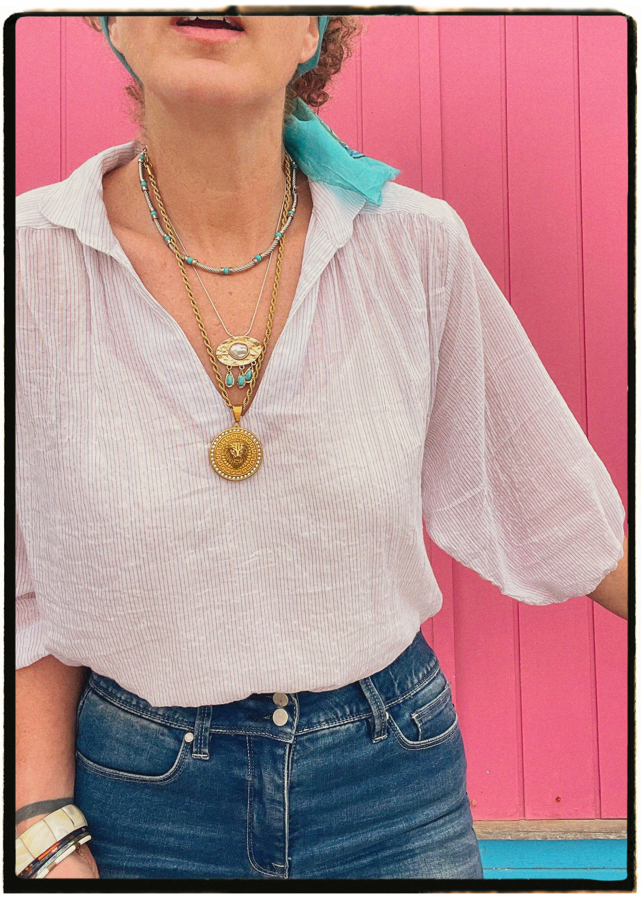 Person wearing a white blouse with ruffled sleeves and blue jeans, standing against a pink wall.