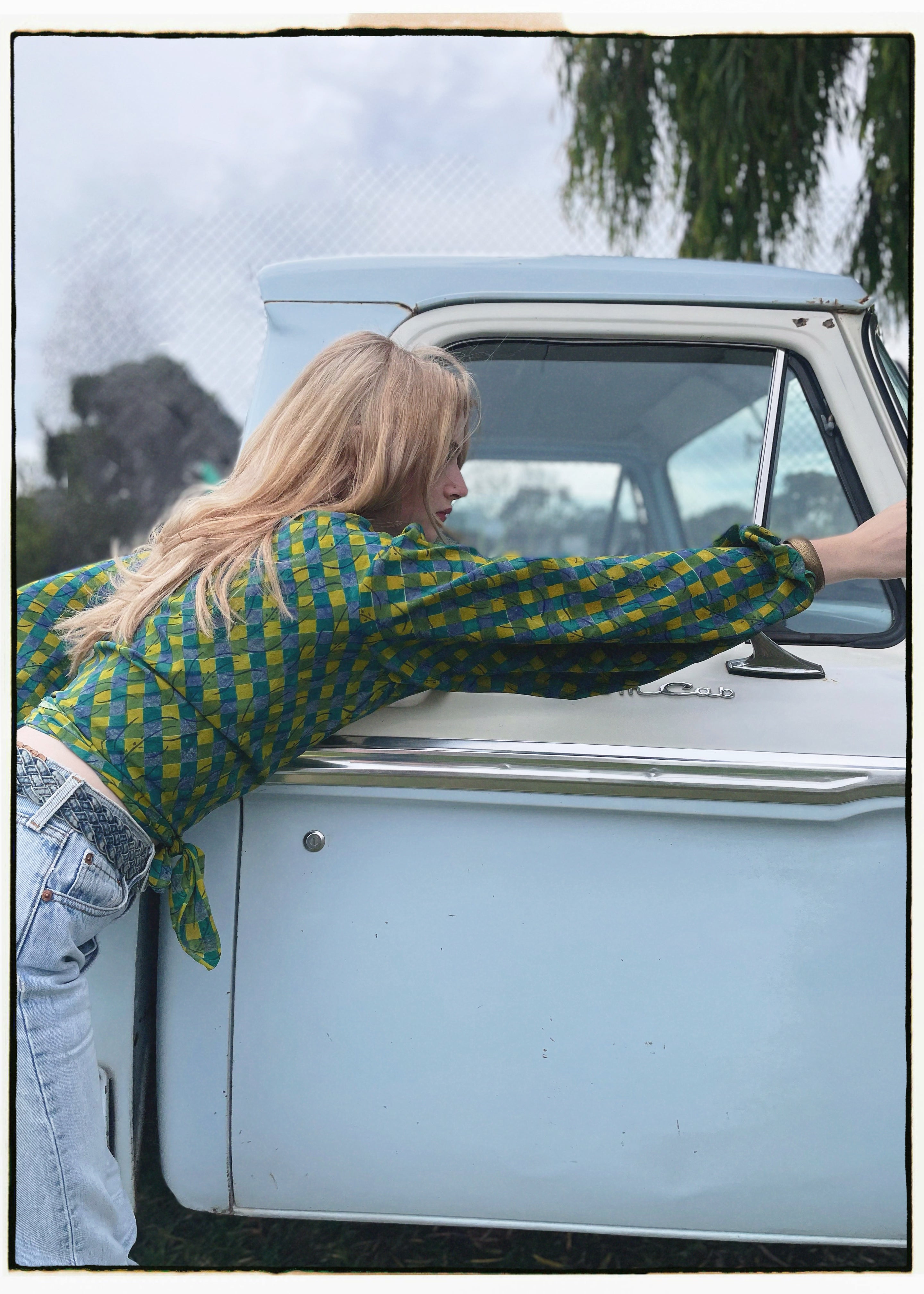 Woman wearing a bohemian style balloon sleeved blouse made from vintage Indian repurposed silk crepe saree sitting in the back of a vintage car with a scenic background
