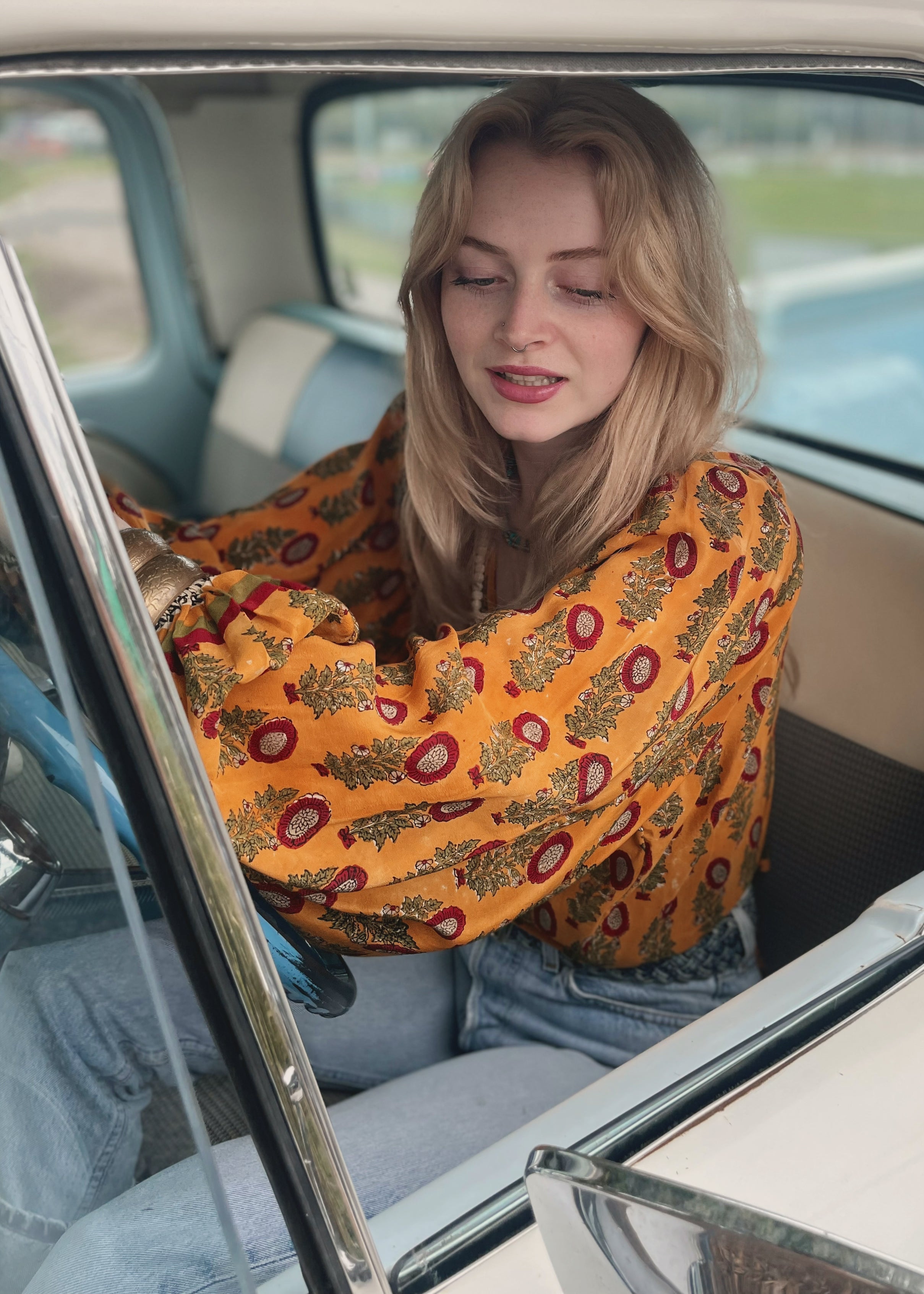 Woman wearing a bohemian style balloon sleeved blouse made from vintage Indian repurposed silk crepe saree sitting in the back of a vintage car with a scenic background