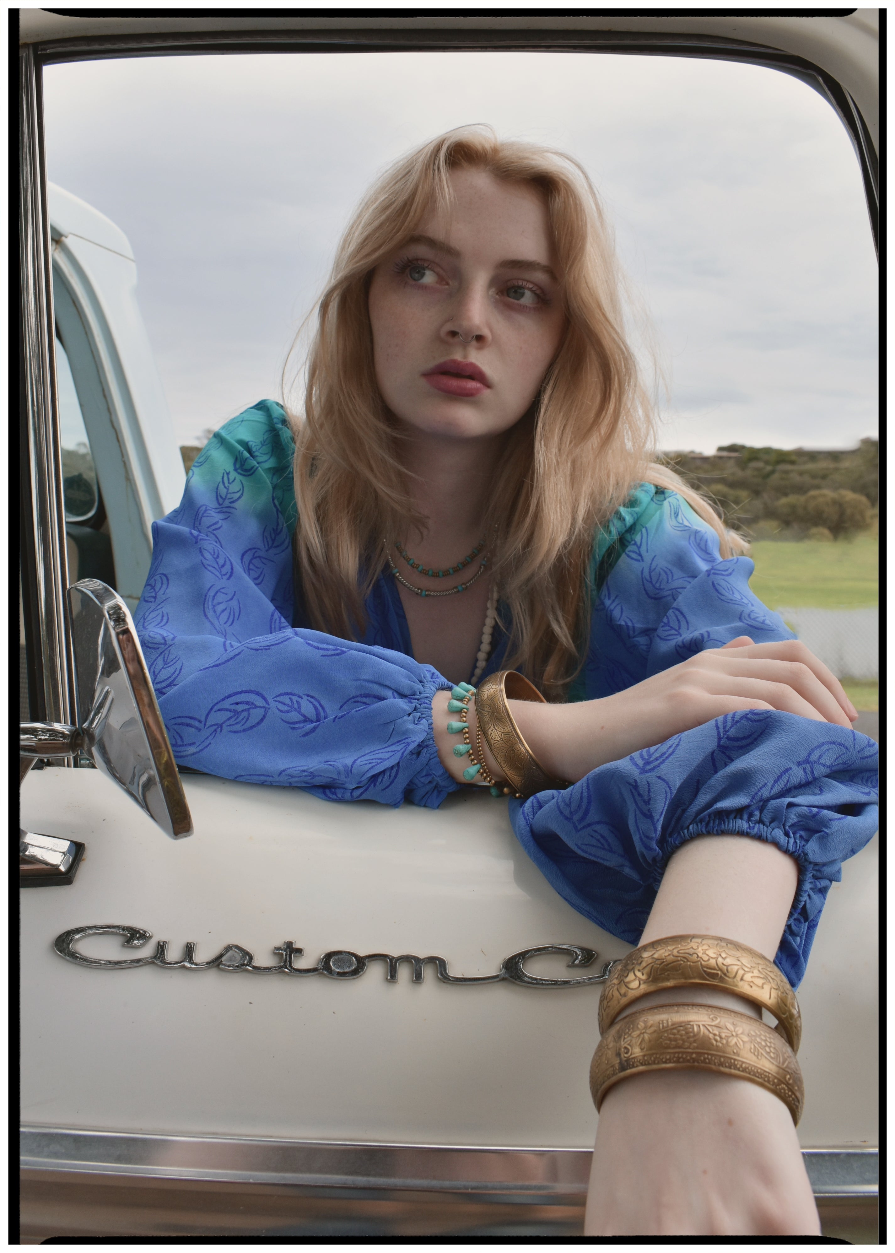 Woman wearing a bohemian style balloon sleeved blouse made from vintage Indian repurposed silk crepe saree sitting in the back of a vintage car with a scenic background