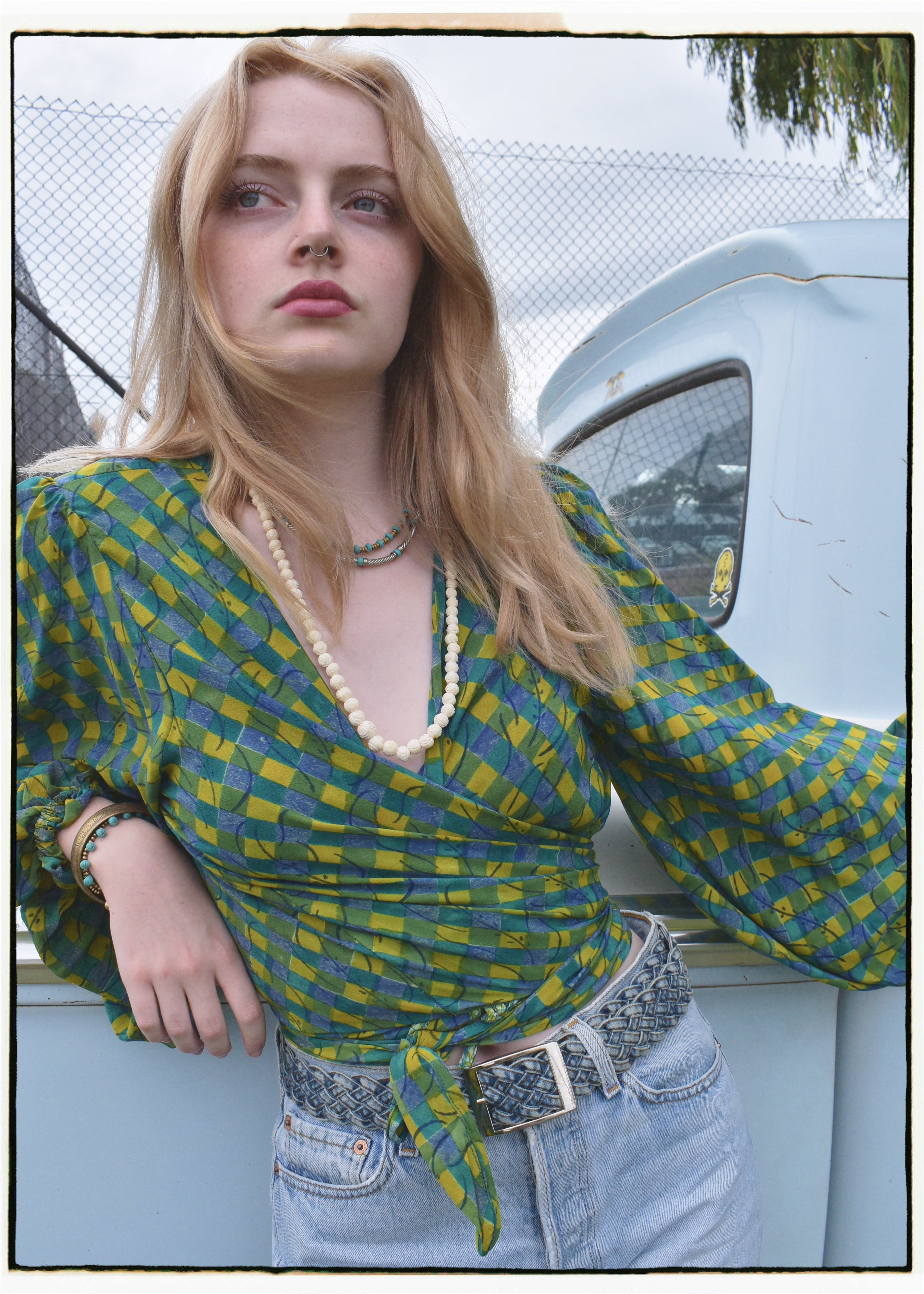 Woman wearing a bohemian style balloon sleeved blouse made from vintage Indian repurposed silk crepe saree sitting in the back of a vintage car with a scenic background