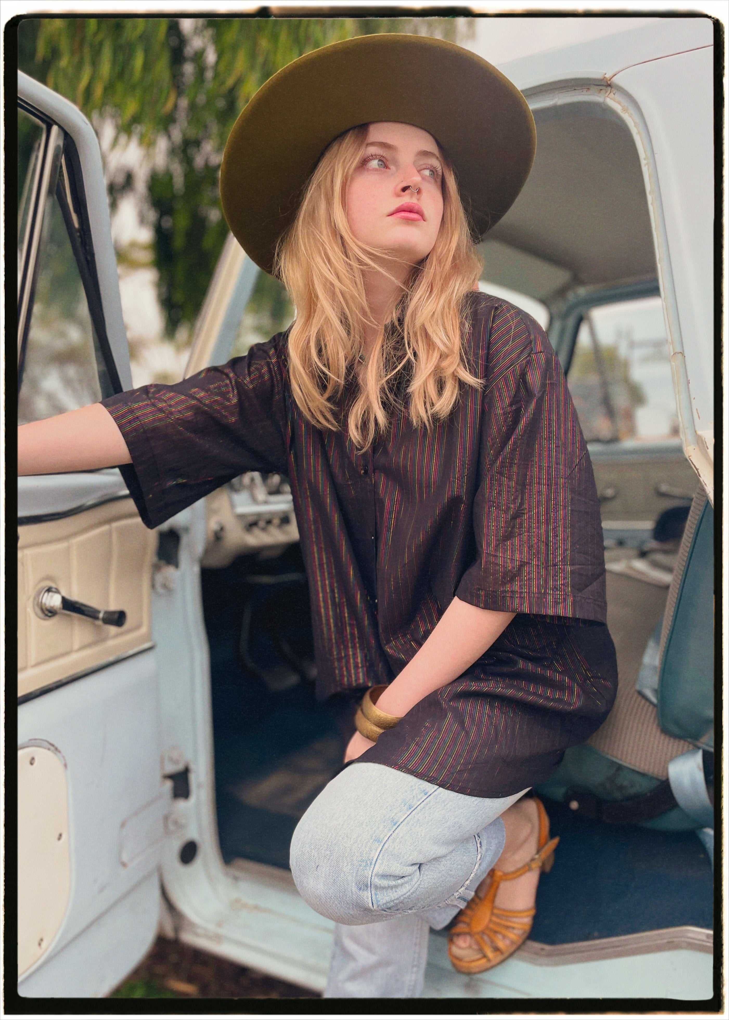 Woman wearing a bohemian style balloon sleeved blouse made from vintage Indian repurposed silk crepe saree sitting in the back of a vintage car with a scenic background