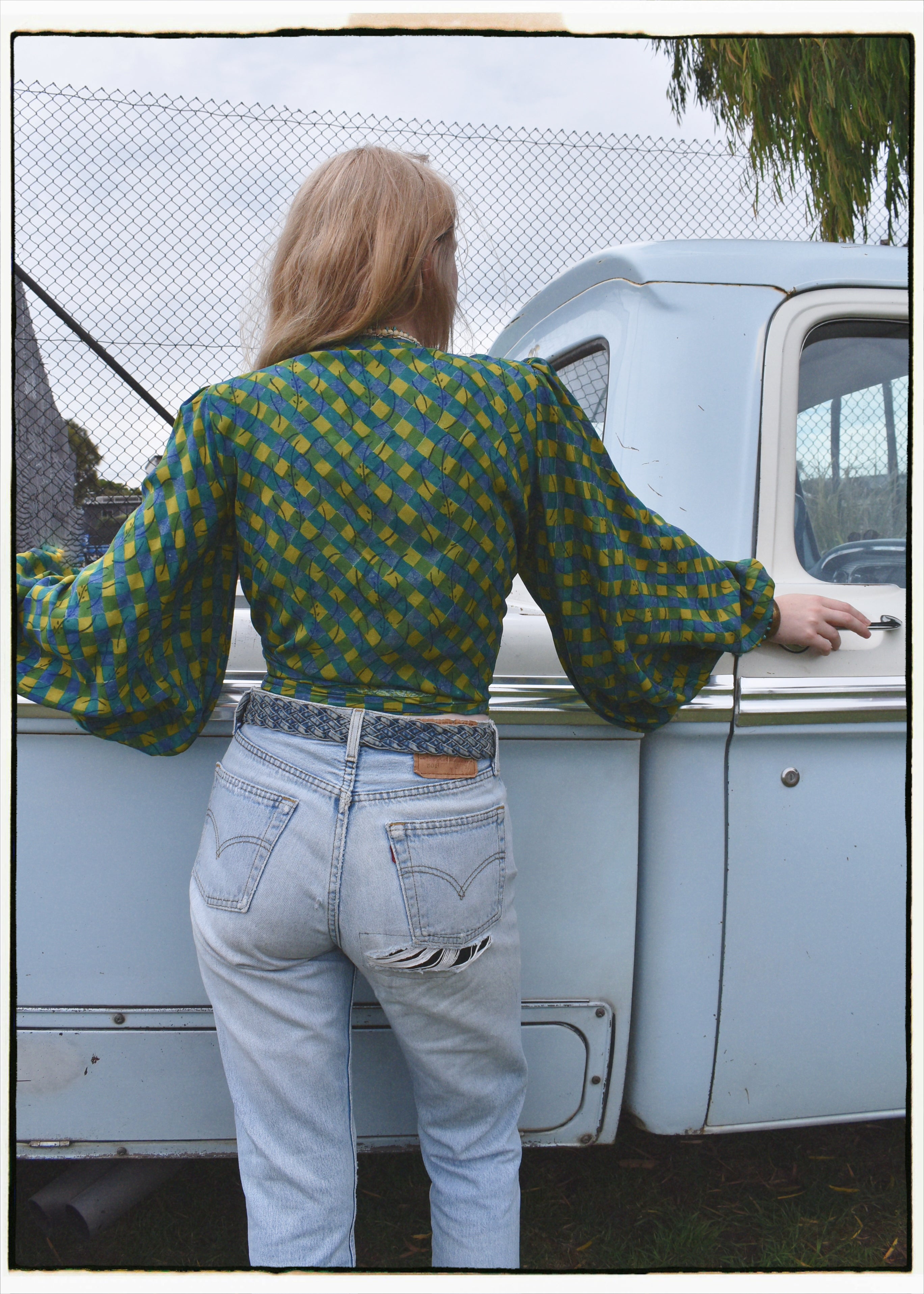 Woman wearing a bohemian style balloon sleeved blouse made from vintage Indian repurposed silk crepe saree sitting in the back of a vintage car with a scenic background