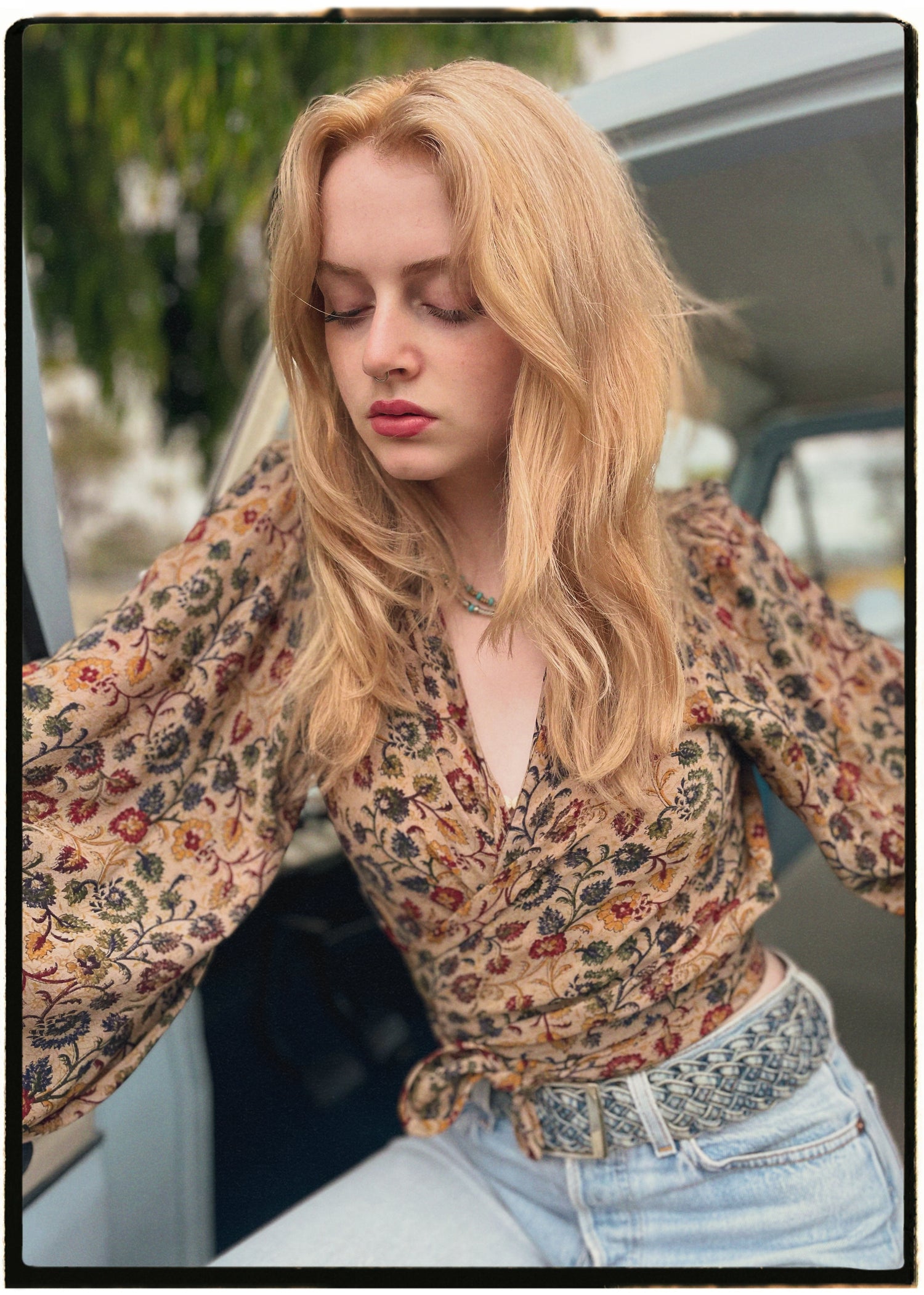 Woman wearing a bohemian style balloon sleeved blouse made from vintage Indian repurposed silk crepe saree sitting in the back of a vintage car with a scenic background