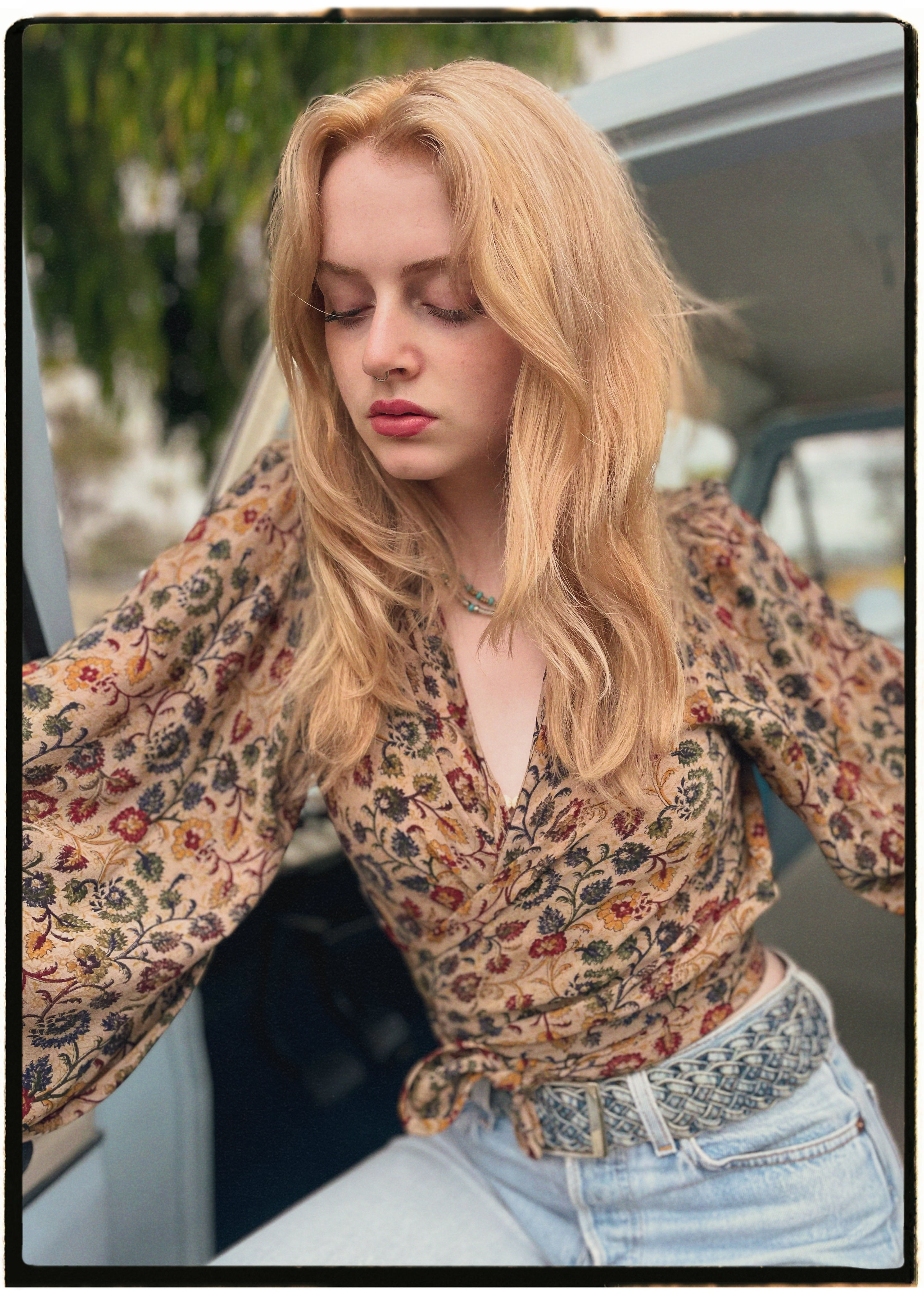 Woman wearing a bohemian style balloon sleeved blouse made from vintage Indian repurposed silk crepe saree sitting in the back of a vintage car with a scenic background