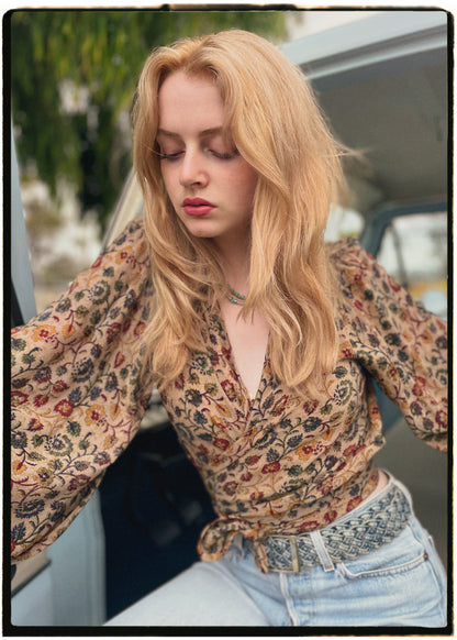 Woman wearing a bohemian style balloon sleeved blouse made from vintage Indian repurposed silk crepe saree sitting in the back of a vintage car with a scenic background