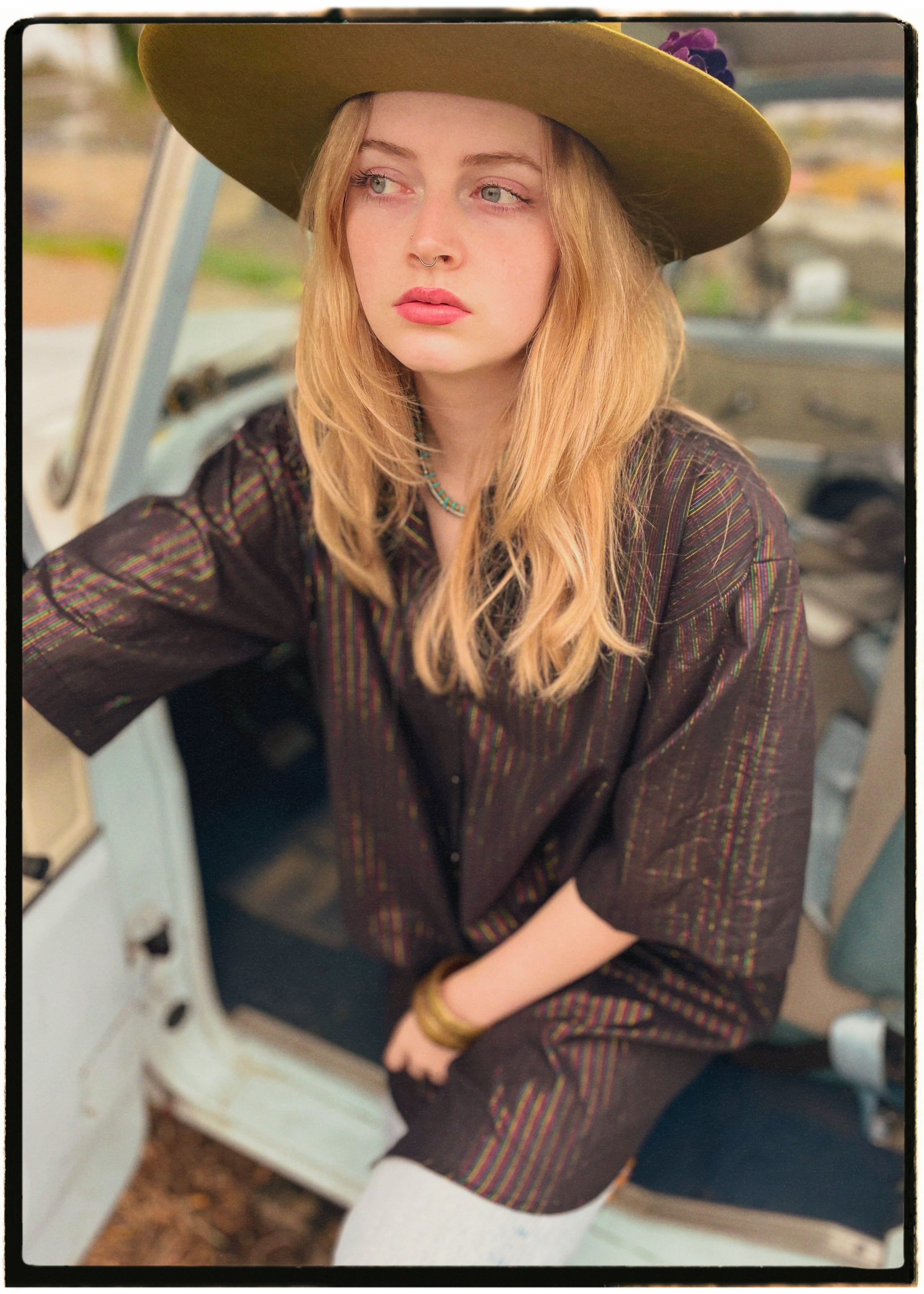Woman wearing a bohemian style balloon sleeved blouse made from vintage Indian repurposed silk crepe saree sitting in the back of a vintage car with a scenic background