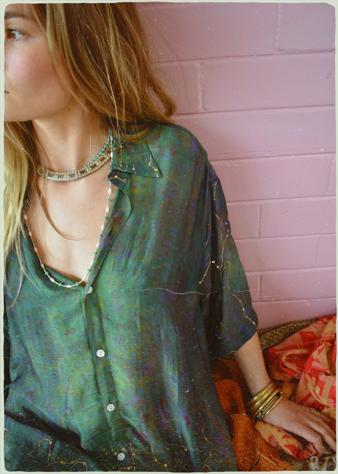 Person wearing a green patterned shirt against a pink tiled wall.