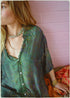 Person wearing a green patterned shirt against a pink tiled wall.