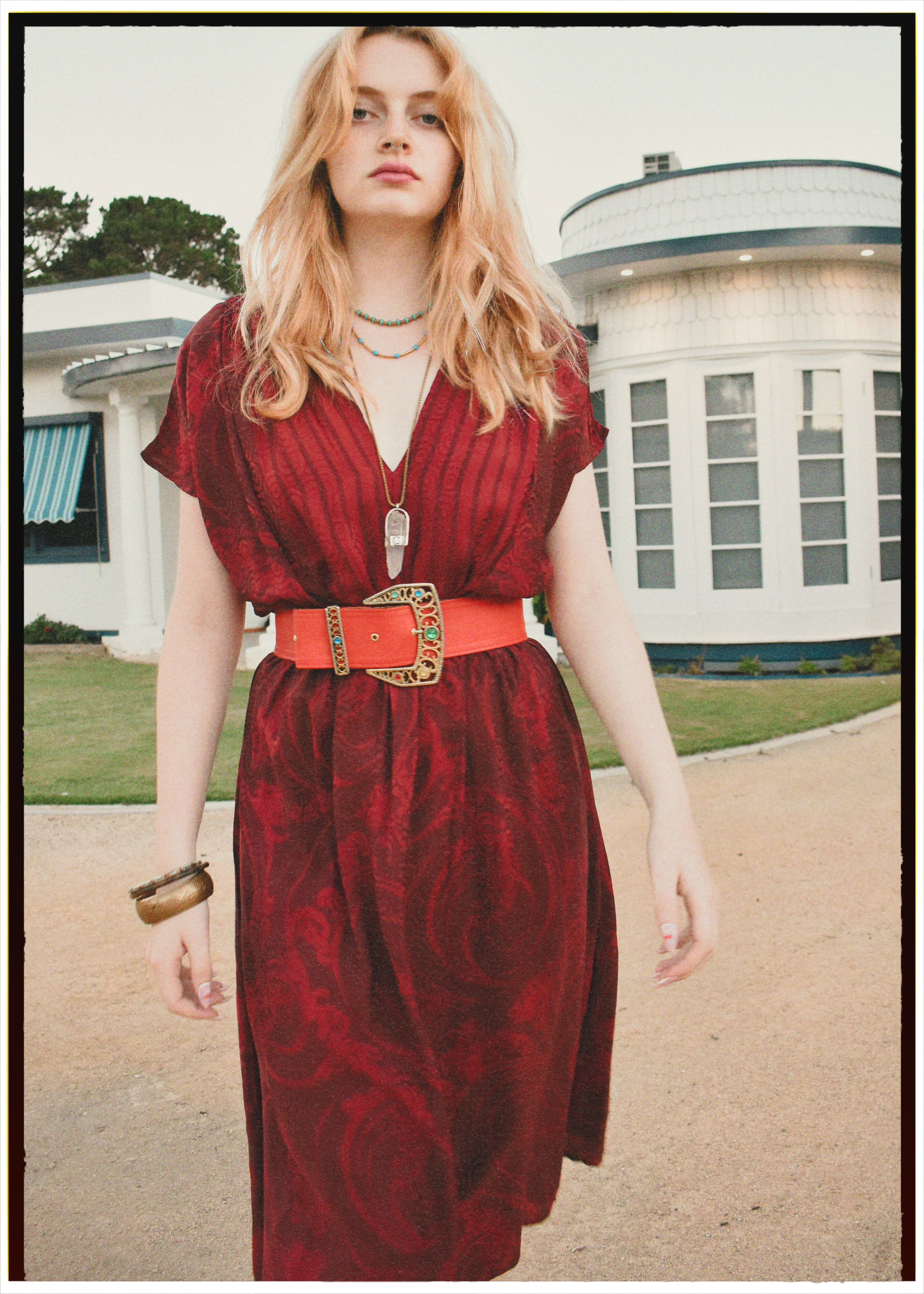 Woman in a red dress with a belt standing in front of a building.