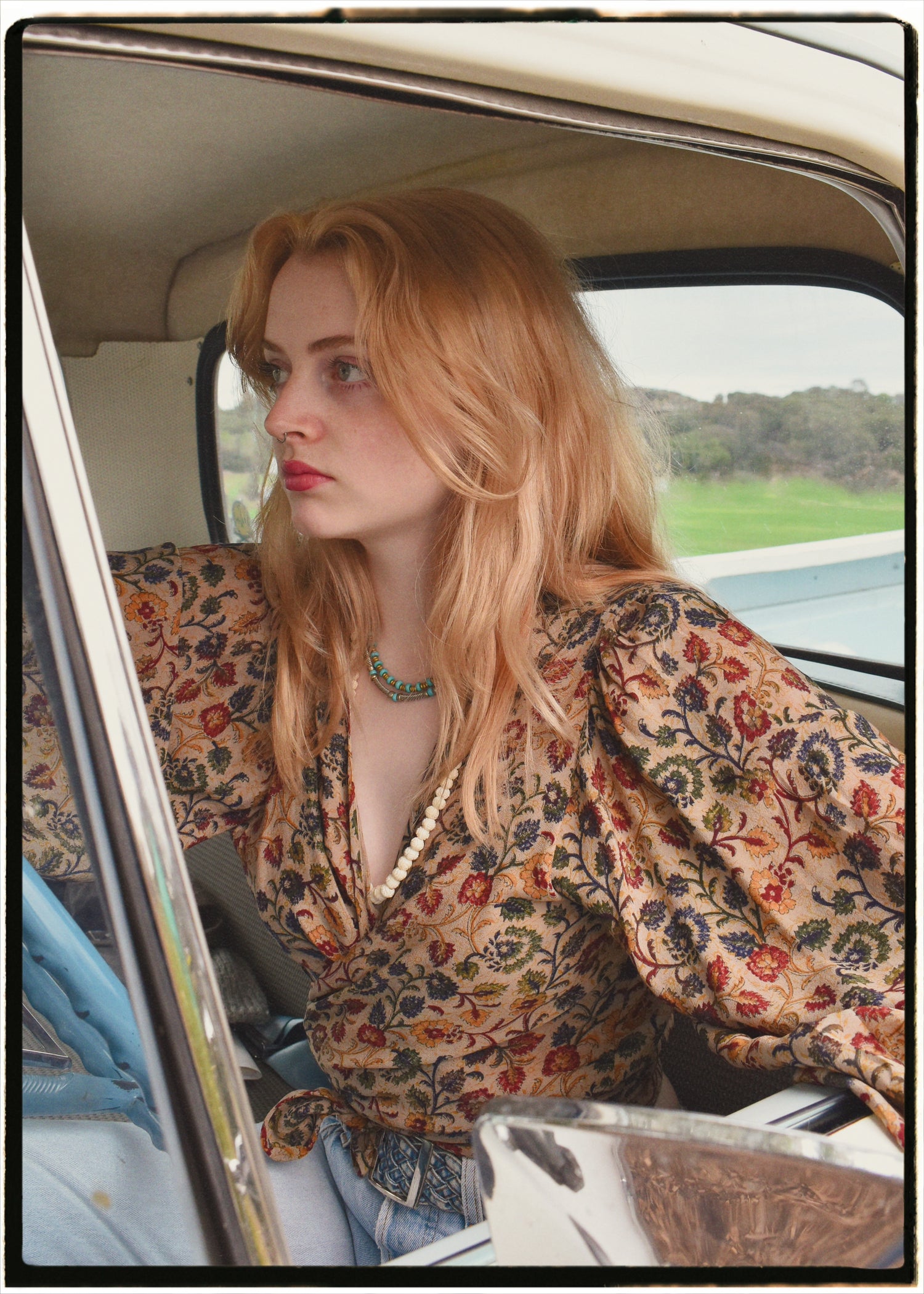 Woman wearing a bohemian style balloon sleeved blouse made from vintage Indian repurposed silk crepe saree sitting in the back of a vintage car with a scenic background