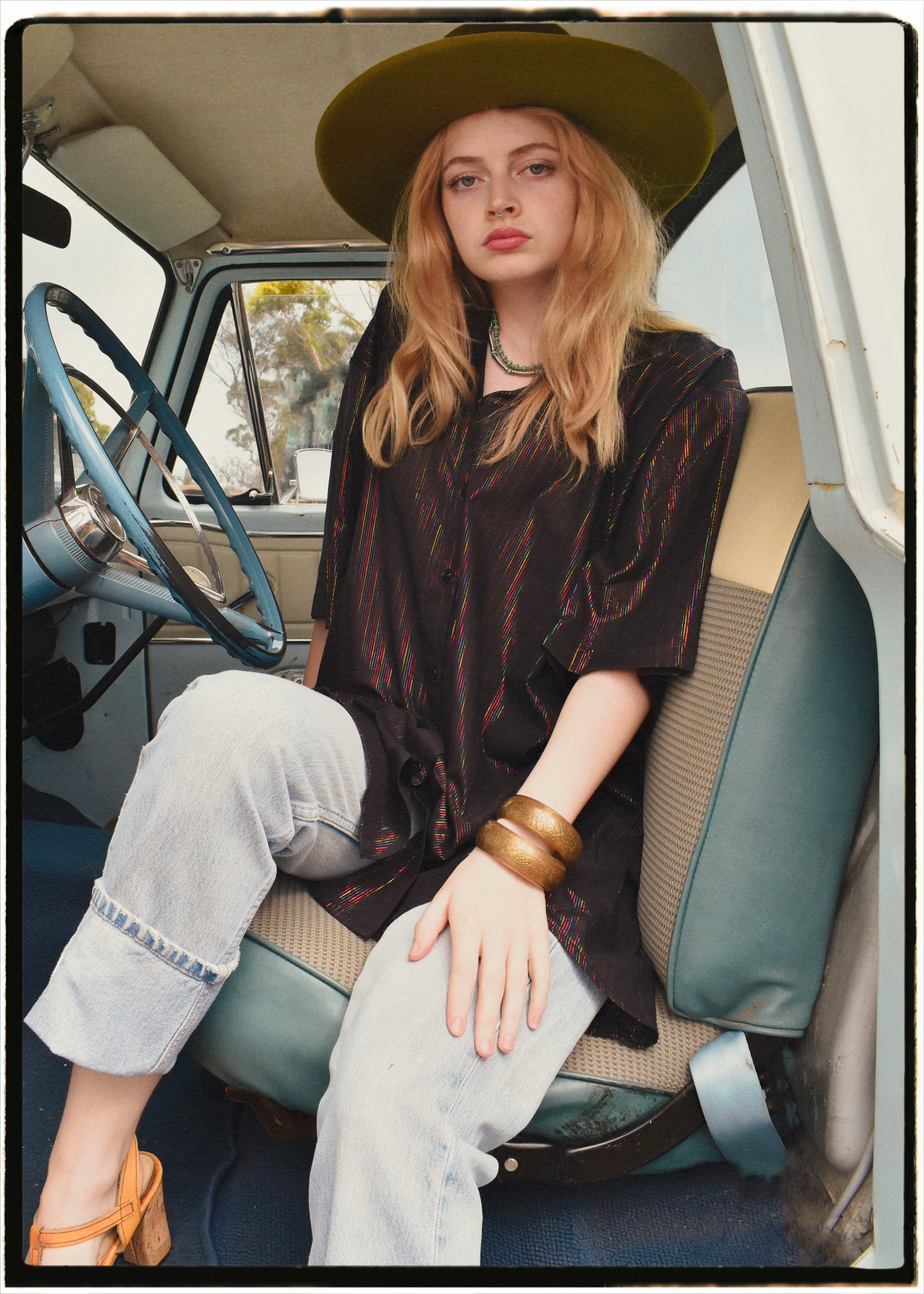 Woman wearing a bohemian style balloon sleeved blouse made from vintage Indian repurposed silk crepe saree sitting in the back of a vintage car with a scenic background