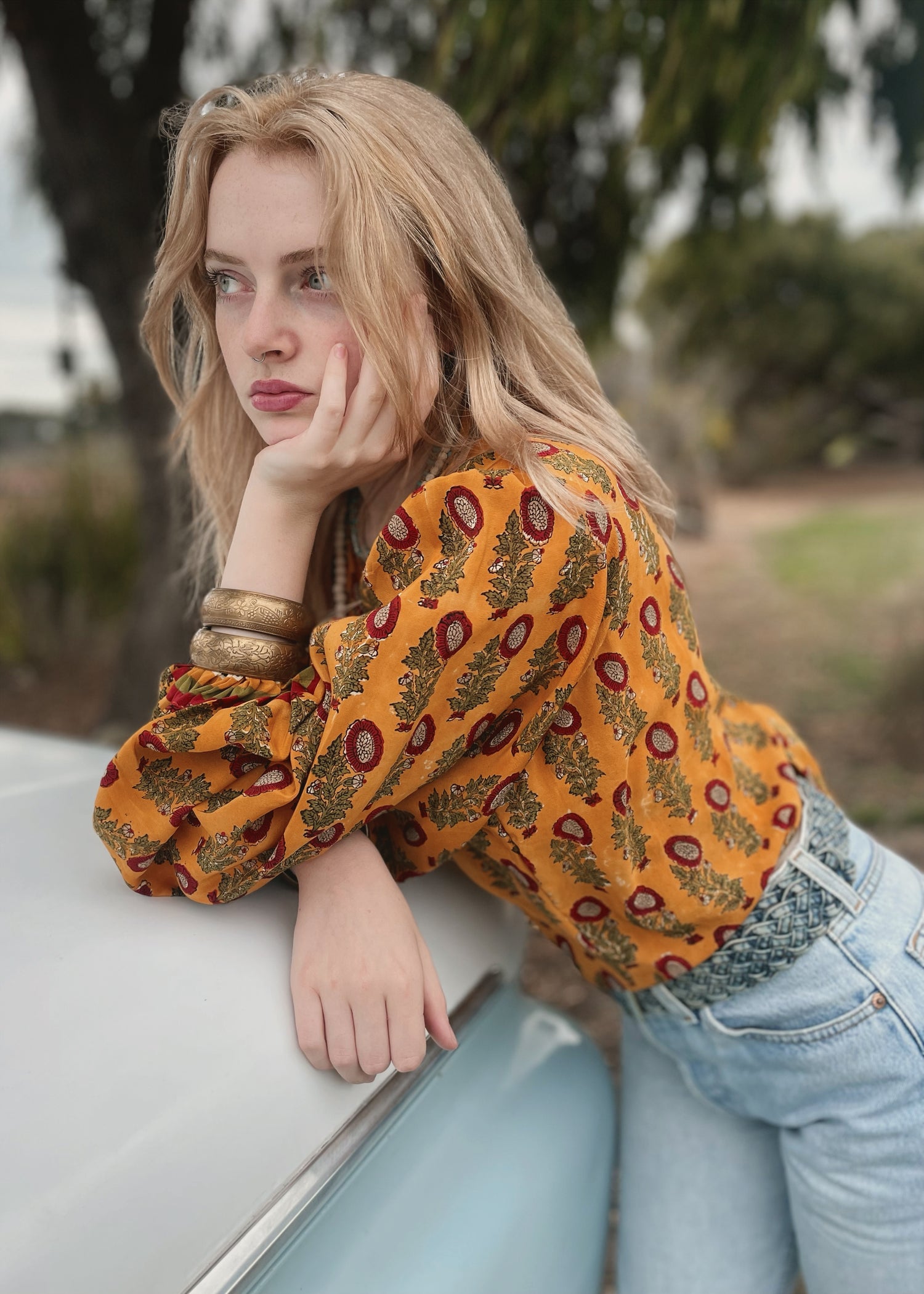 Woman wearing a bohemian style balloon sleeved blouse made from vintage Indian repurposed silk crepe saree sitting in the back of a vintage car with a scenic background