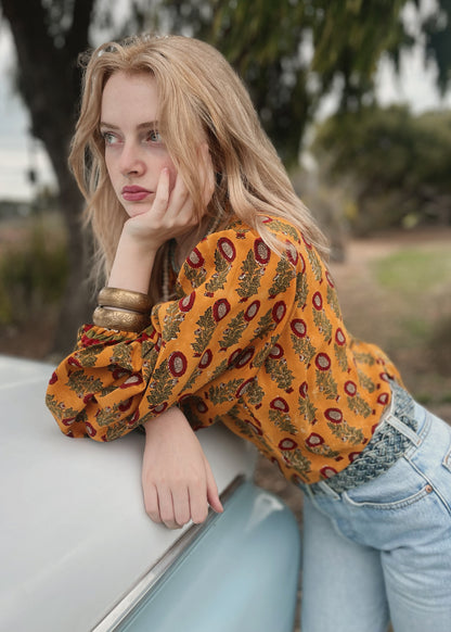 Woman wearing a bohemian style balloon sleeved blouse made from vintage Indian repurposed silk crepe saree sitting in the back of a vintage car with a scenic background