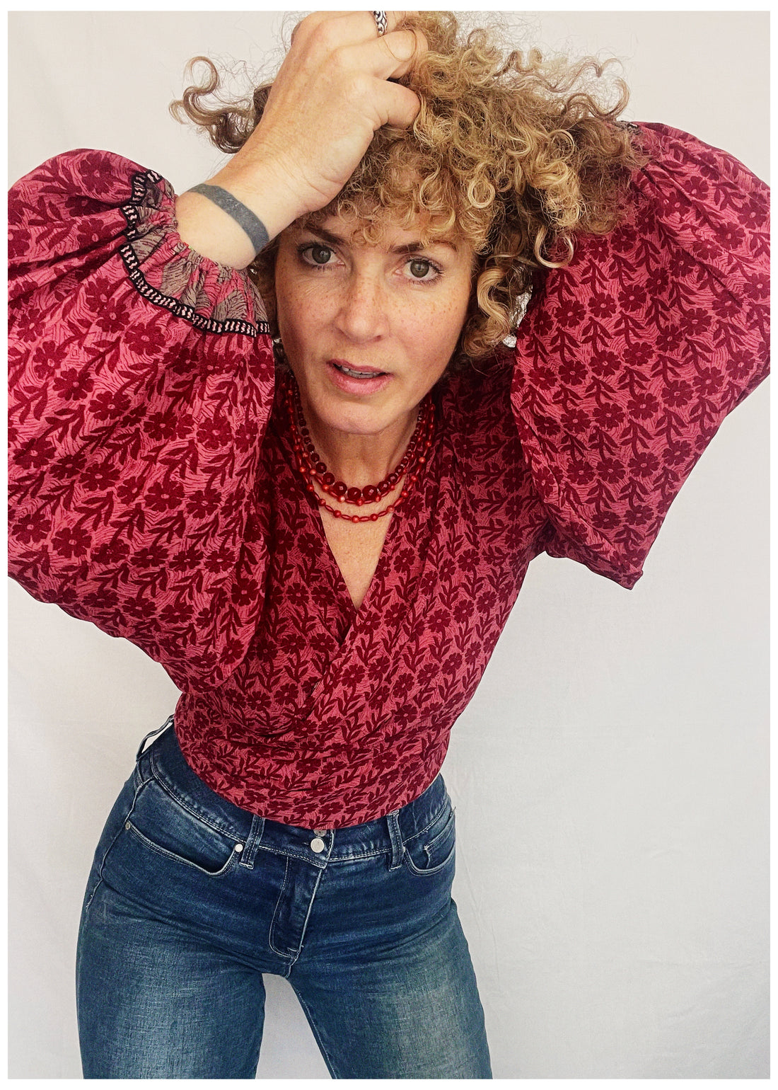 Person wearing a red patterned blouse and blue jeans against a plain background