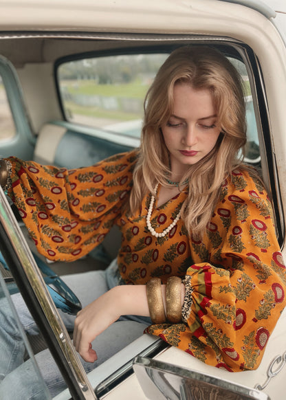 Woman wearing a bohemian style balloon sleeved blouse made from vintage Indian repurposed silk crepe saree sitting in the back of a vintage car with a scenic background