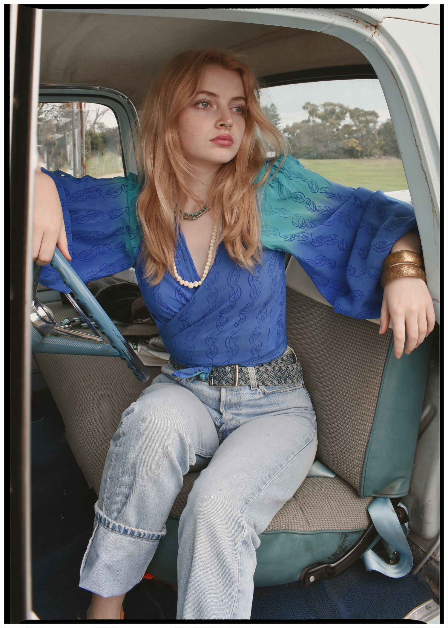 Woman wearing a bohemian style balloon sleeved blouse made from vintage Indian repurposed silk crepe saree sitting in the back of a vintage car with a scenic background