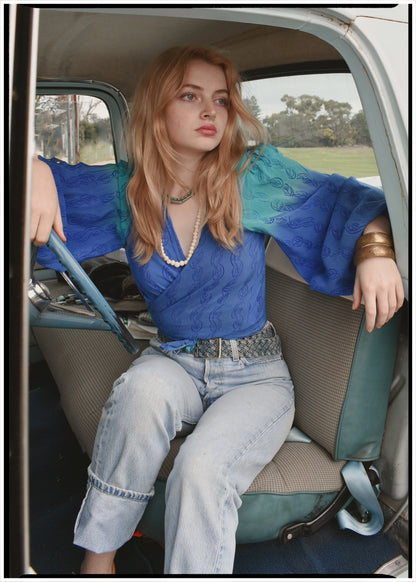 Woman wearing a bohemian style balloon sleeved blouse made from vintage Indian repurposed silk crepe saree sitting in the back of a vintage car with a scenic background