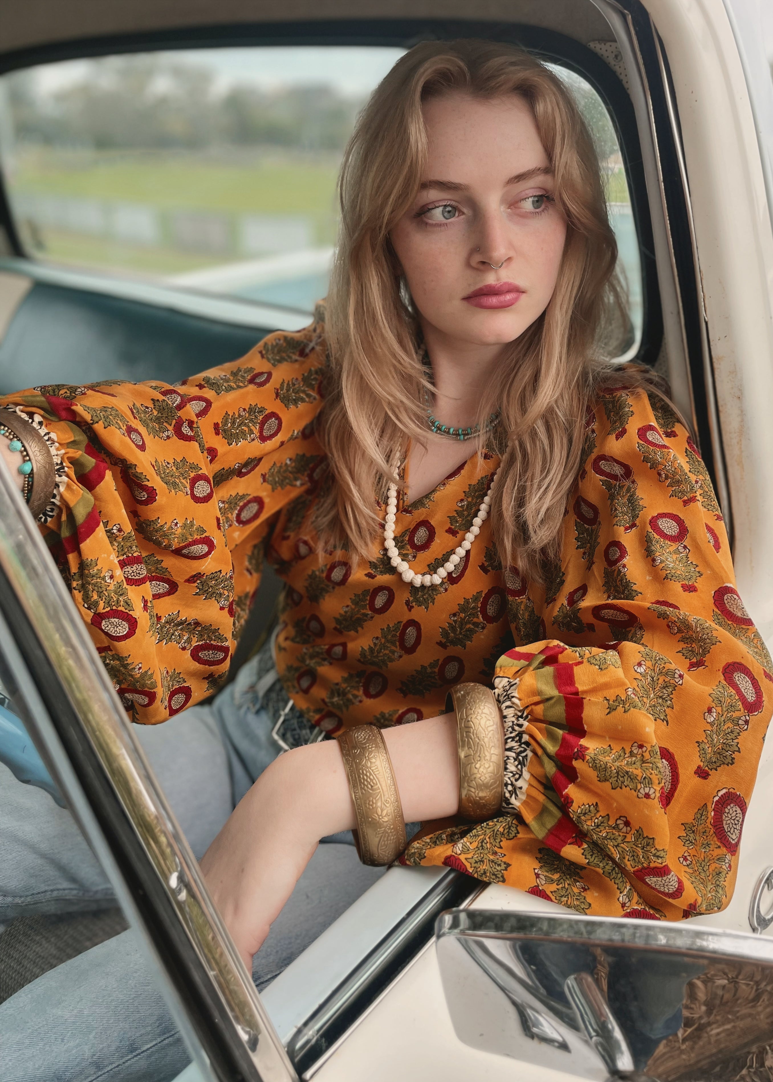 Woman wearing a bohemian style balloon sleeved blouse made from vintage Indian repurposed silk crepe saree sitting in the back of a vintage car with a scenic background