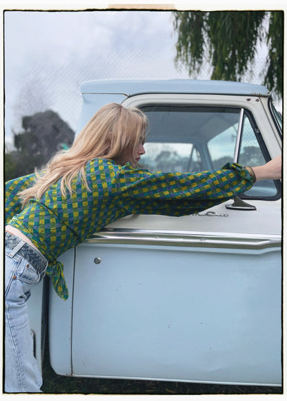 Woman wearing a bohemian style balloon sleeved blouse made from vintage Indian repurposed silk crepe saree sitting in the back of a vintage car with a scenic background