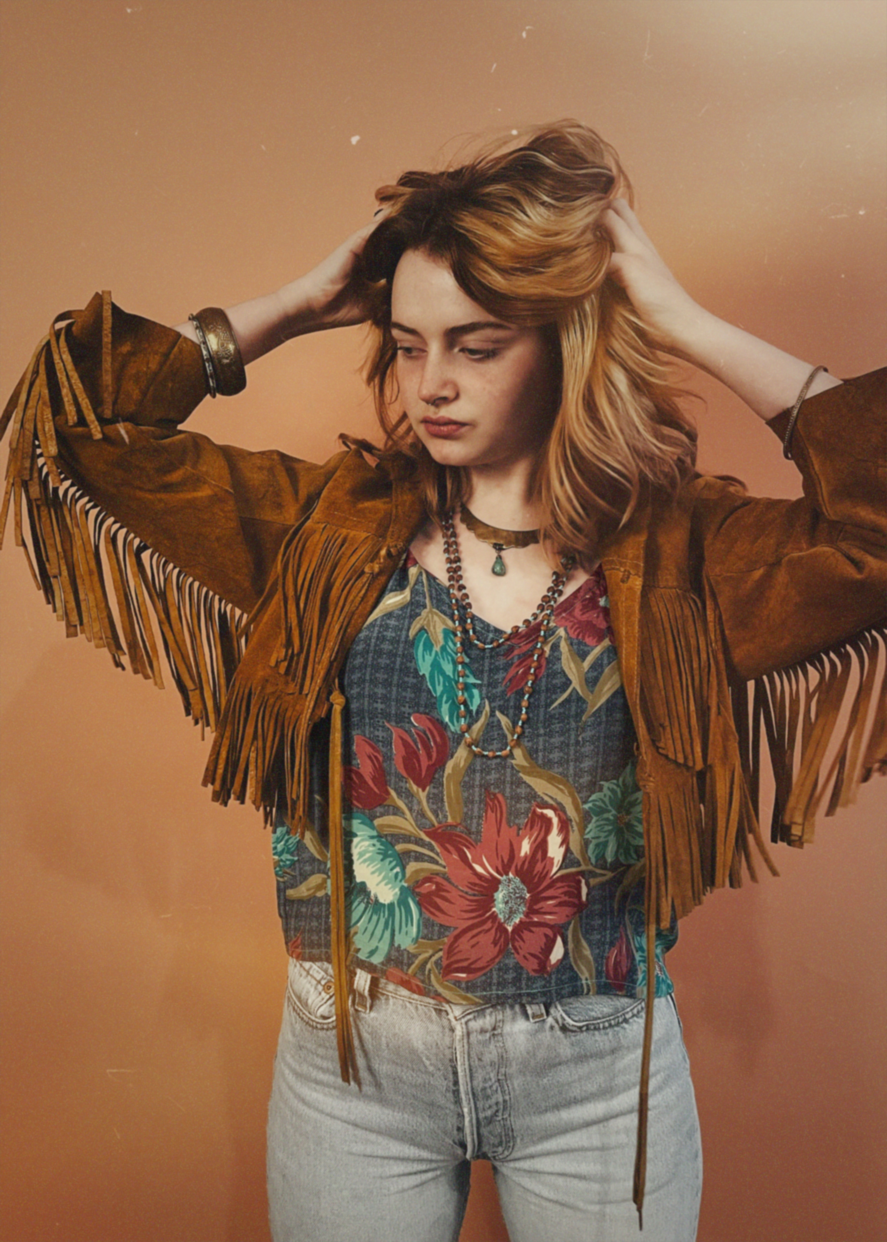 Woman wearing a brown fringed jacket over a colorful floral shirt with a plain background