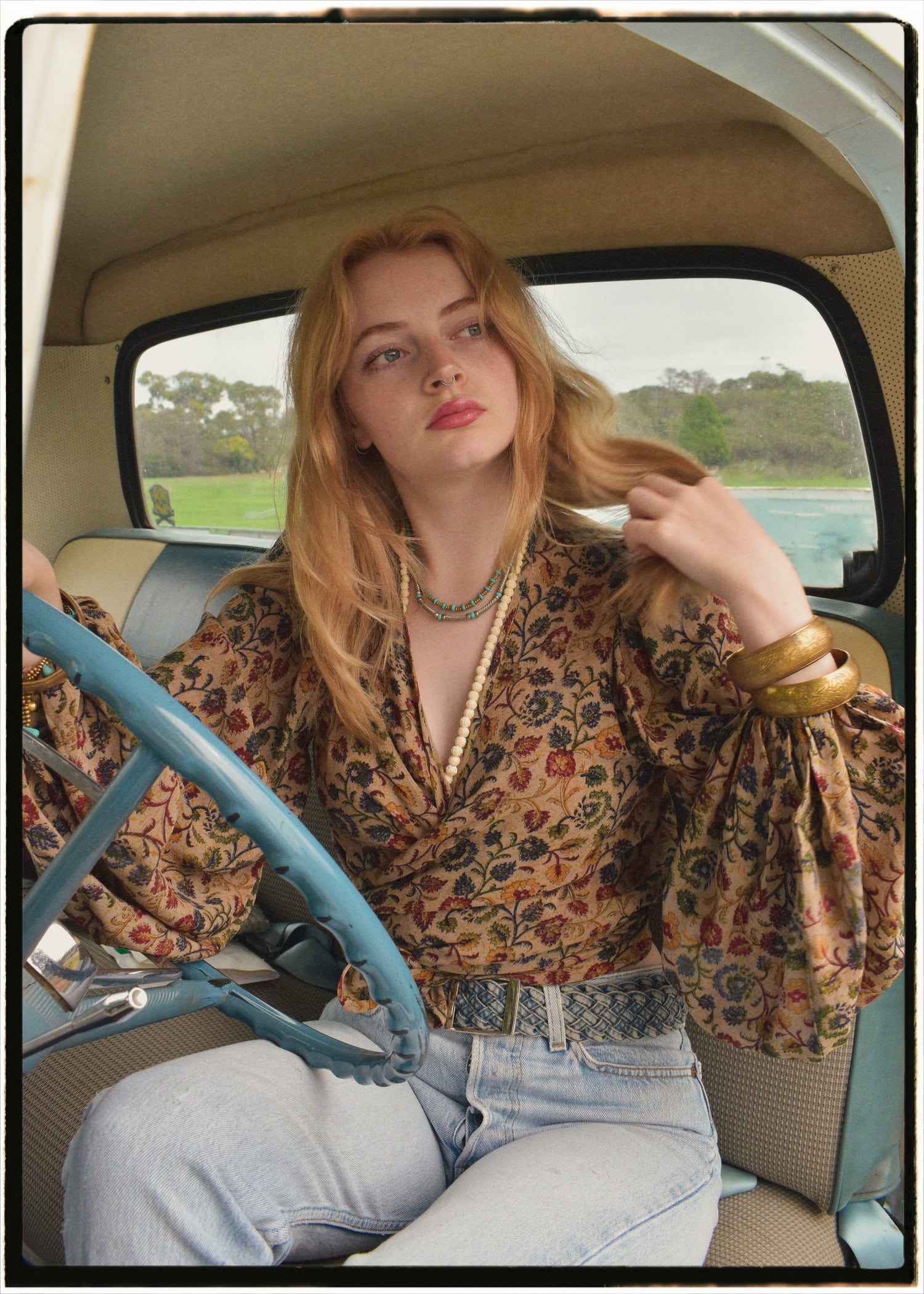 Woman wearing a bohemian style balloon sleeved blouse made from vintage Indian repurposed silk crepe saree sitting in the back of a vintage car with a scenic background