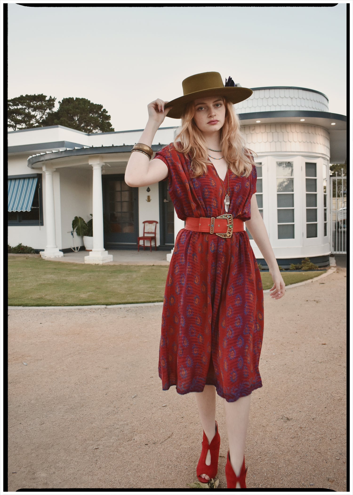 Woman in a red bohemian style dress made from repurposed vintage Indian silk crepe sari and hat standing in front of a house.