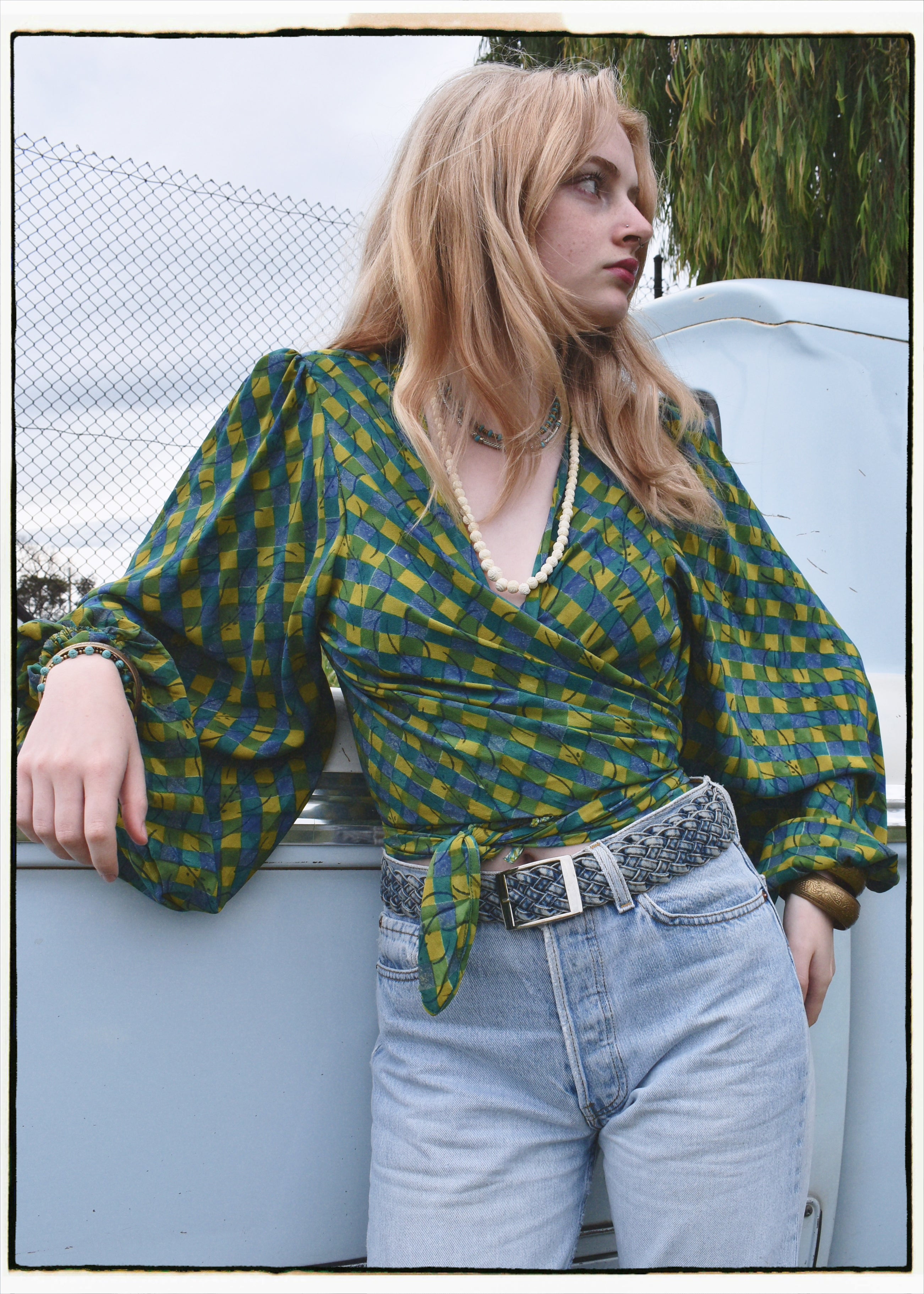 Woman wearing a bohemian style balloon sleeved blouse made from vintage Indian repurposed silk crepe saree sitting in the back of a vintage car with a scenic background