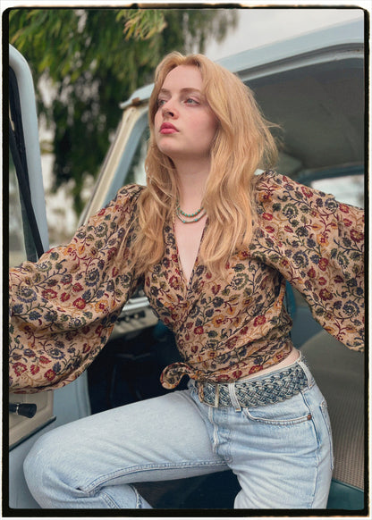Woman wearing a bohemian style balloon sleeved blouse made from vintage Indian repurposed silk crepe saree sitting in the back of a vintage car with a scenic background