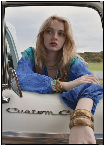 Woman wearing a bohemian style balloon sleeved blouse made from vintage Indian repurposed silk crepe saree sitting in the back of a vintage car with a scenic background
