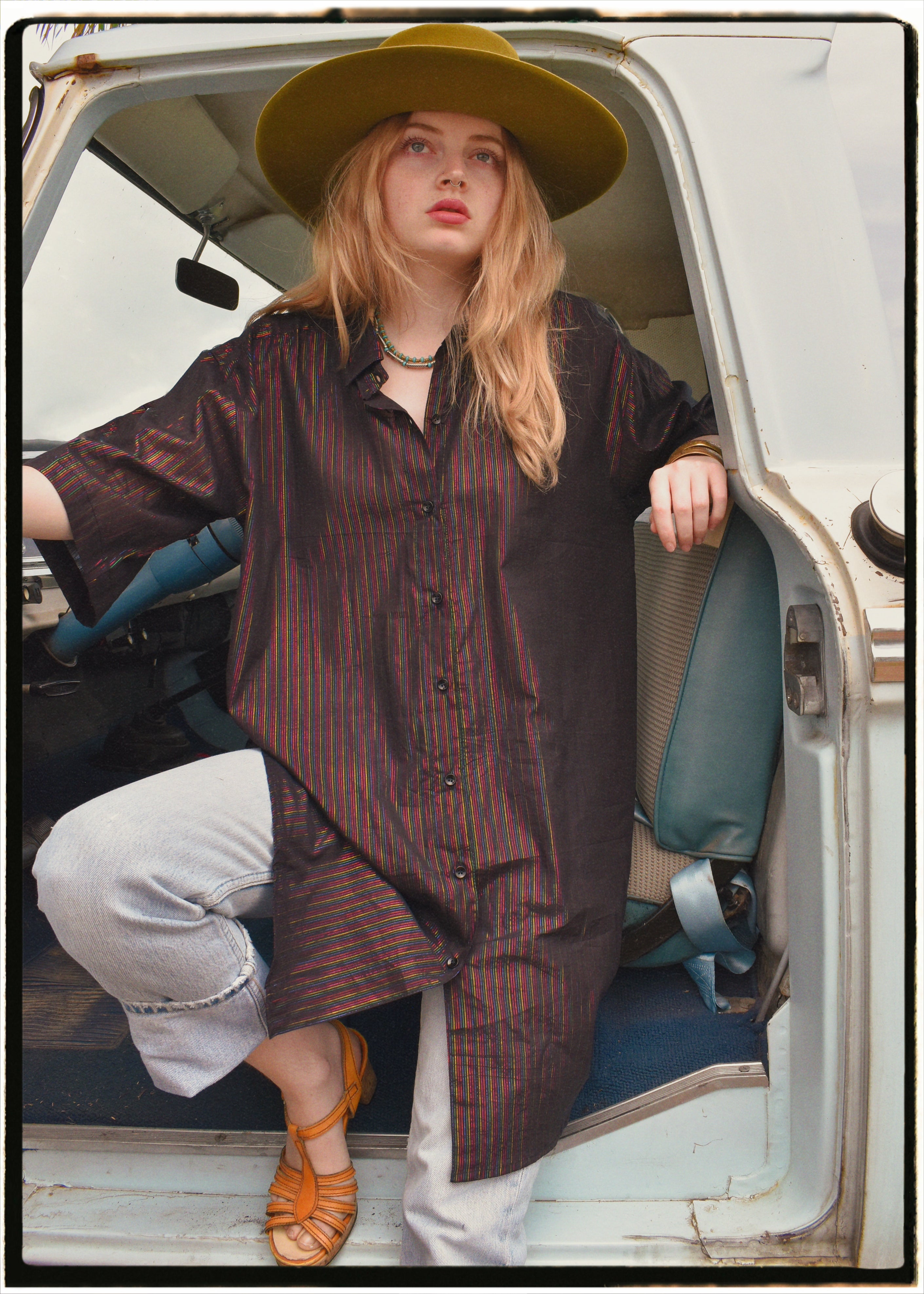 Woman wearing a bohemian style balloon sleeved blouse made from vintage Indian repurposed silk crepe saree sitting in the back of a vintage car with a scenic background