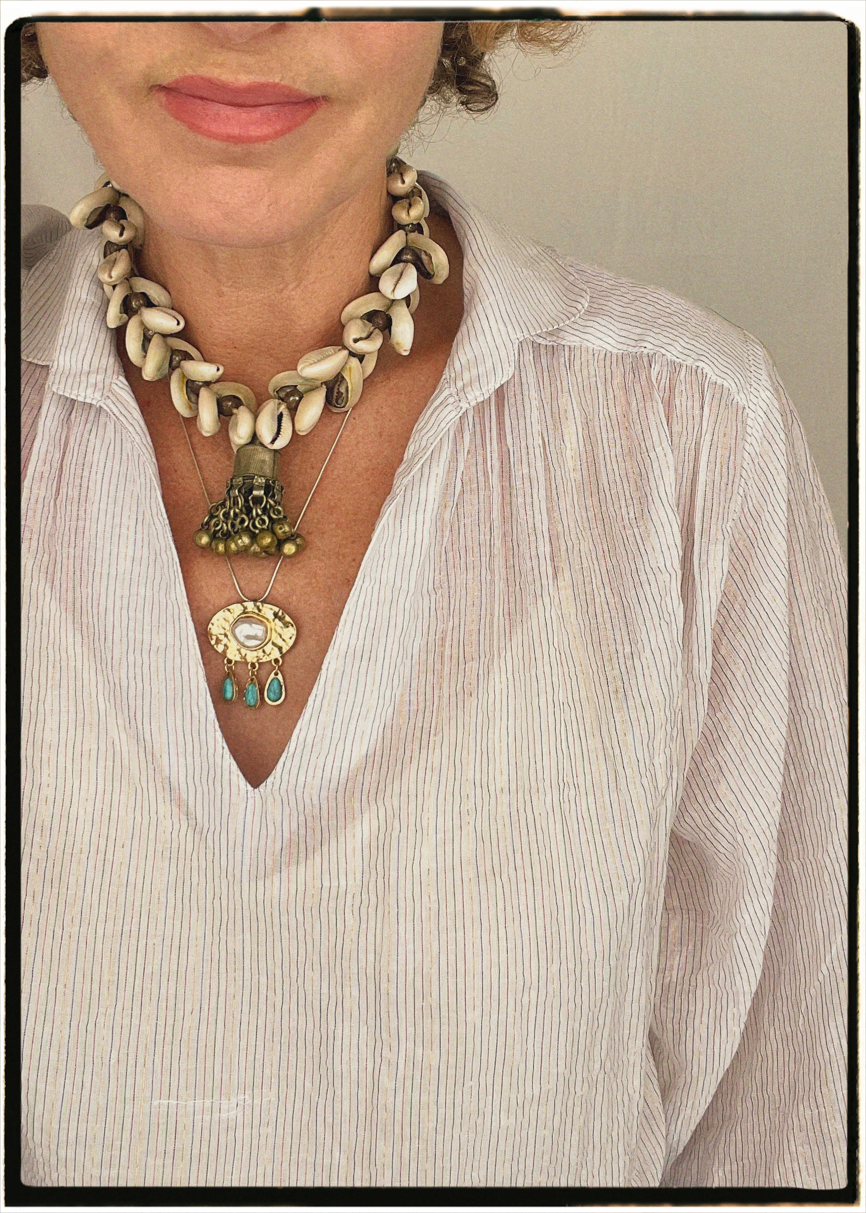 Necklace with shell and pendant worn by a person in a white shirt